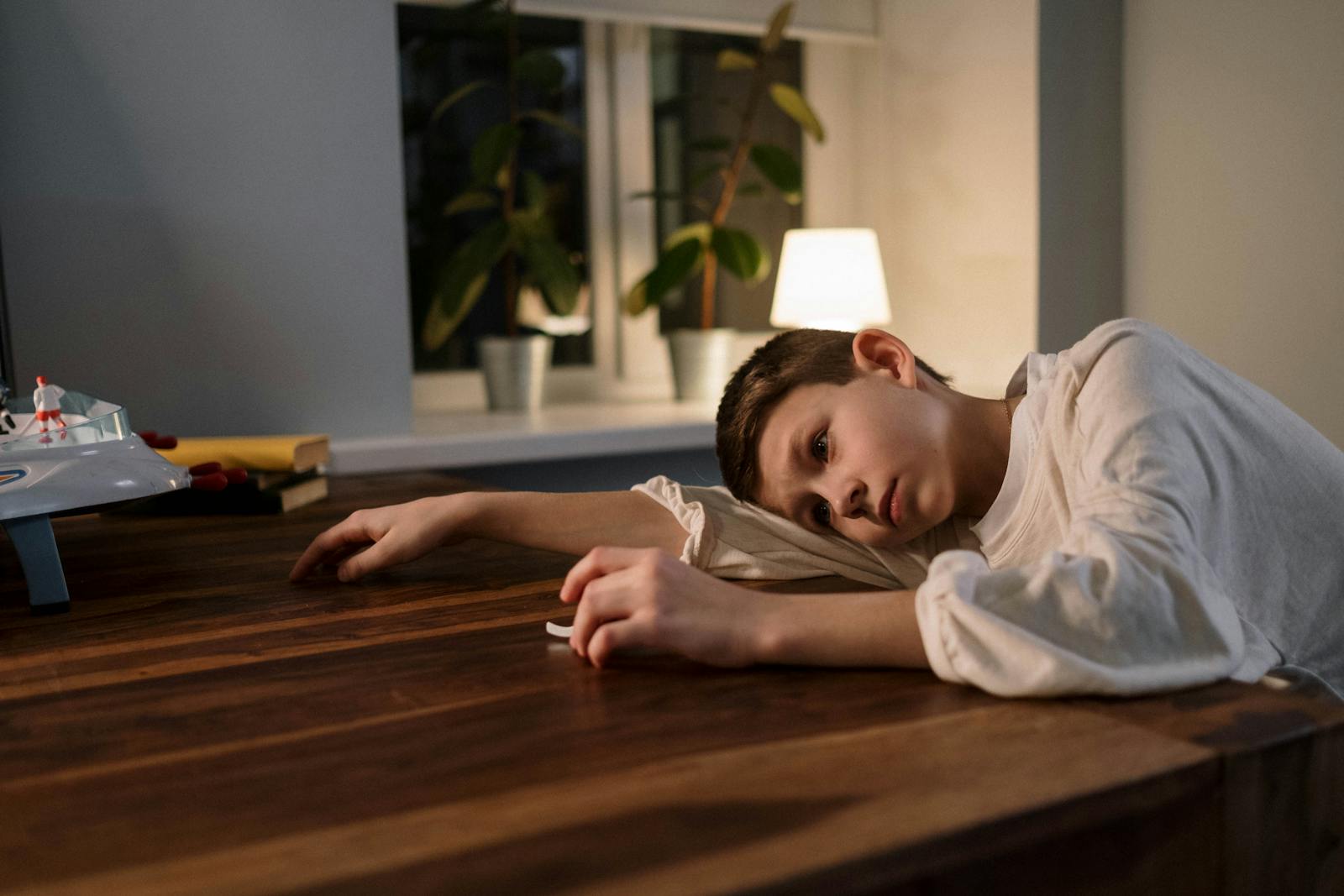 A young boy in thoughtful pose at a table, reflecting emotions indoors. Kids Can't Handle Boredom
