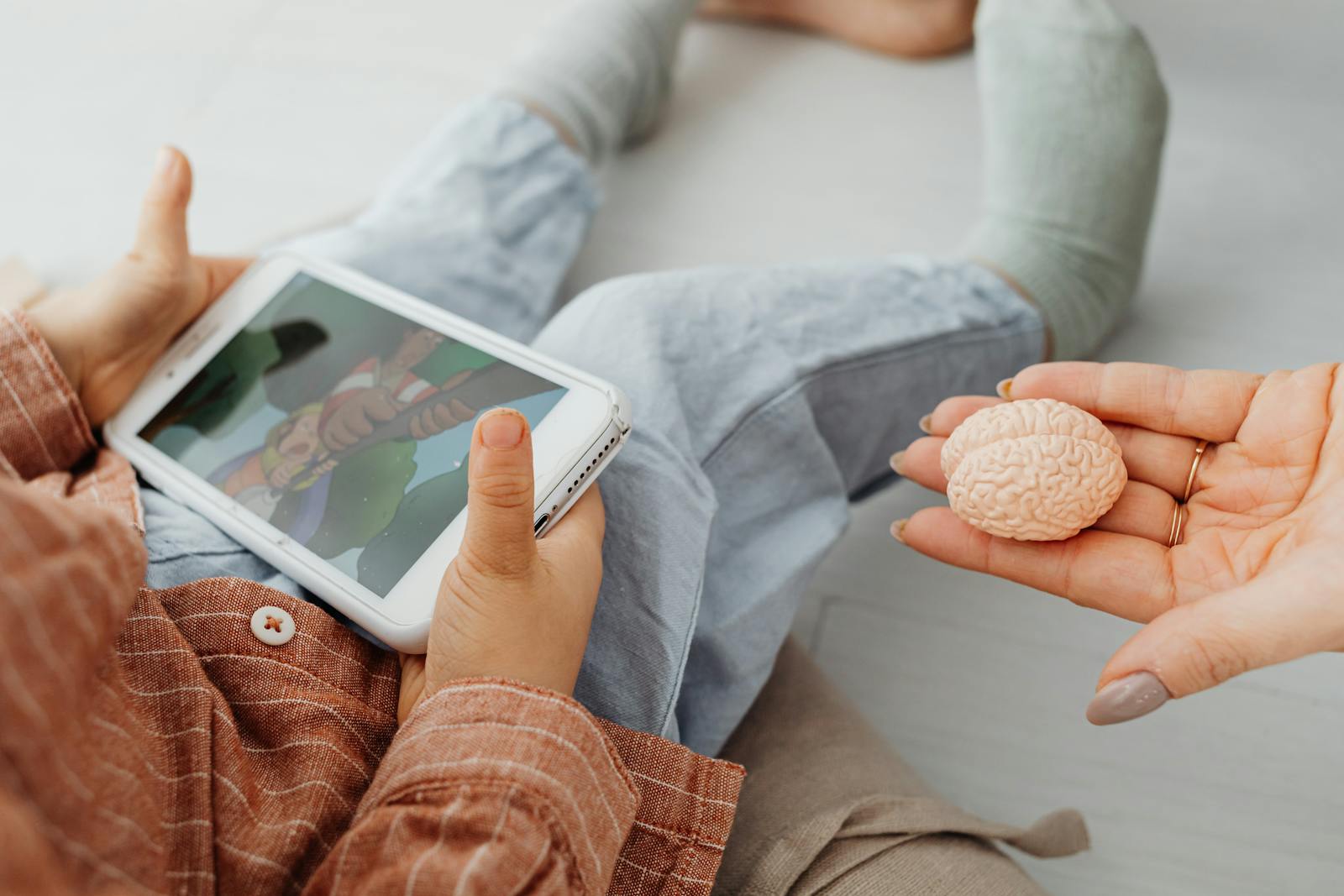 A child watches a cartoon on a tablet as an adult holds a brain model. Short video