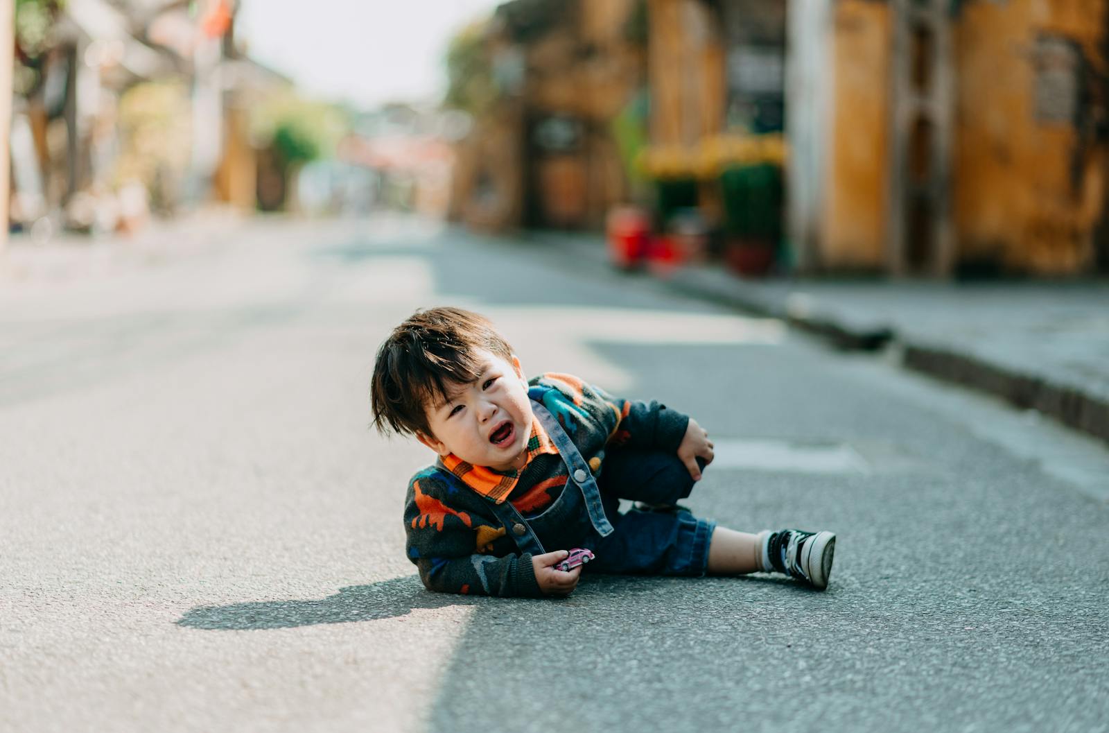 Upset Asian child in casual wear looking at camera after falling on asphalt road on street with residential buildings in town What to Say When Your Child Is Completely Losing It