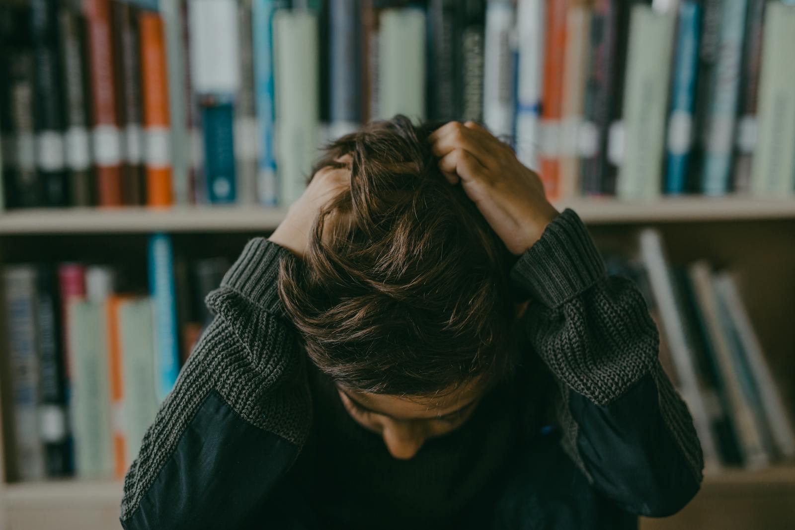 A child appears stressed and frustrated while seated in a library, holding their head. Does My Child Have Anxiety