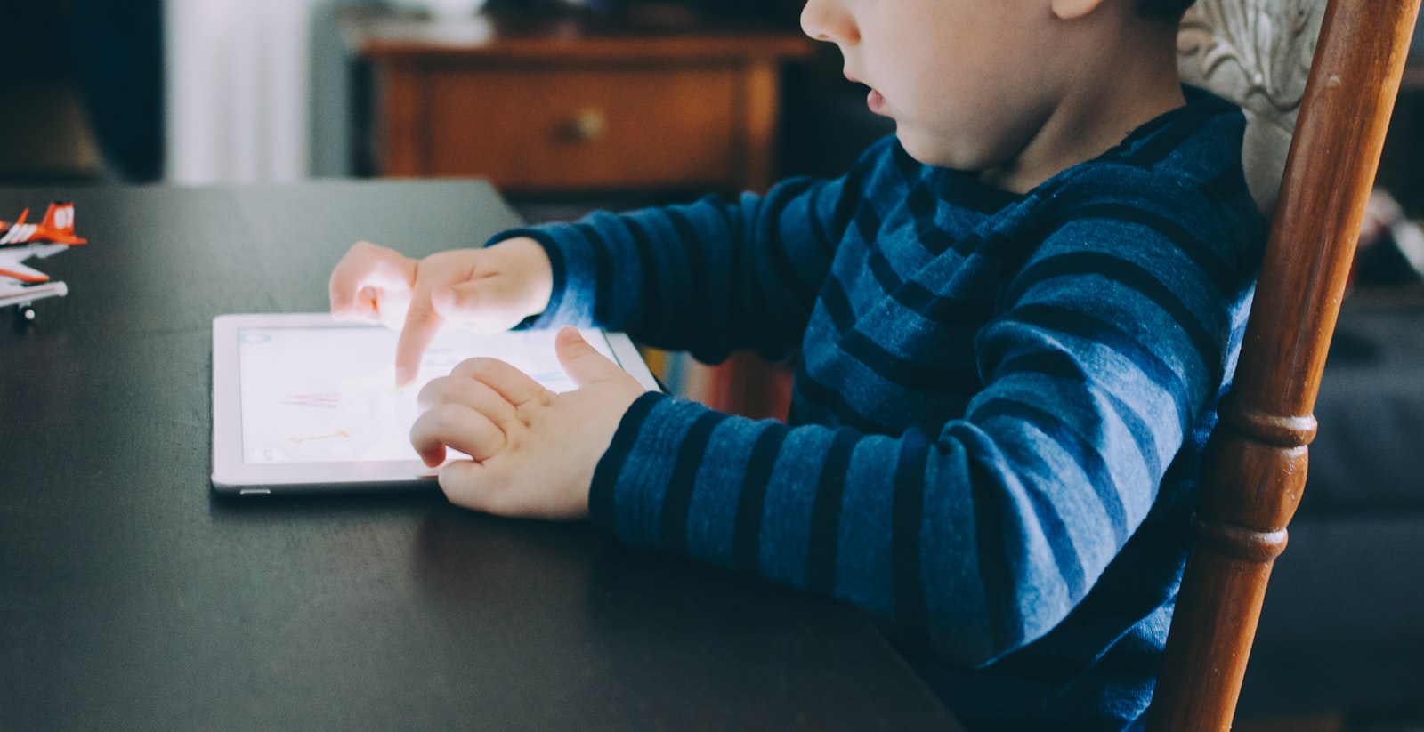 boy sitting on chair beside table using tablet computer screen time