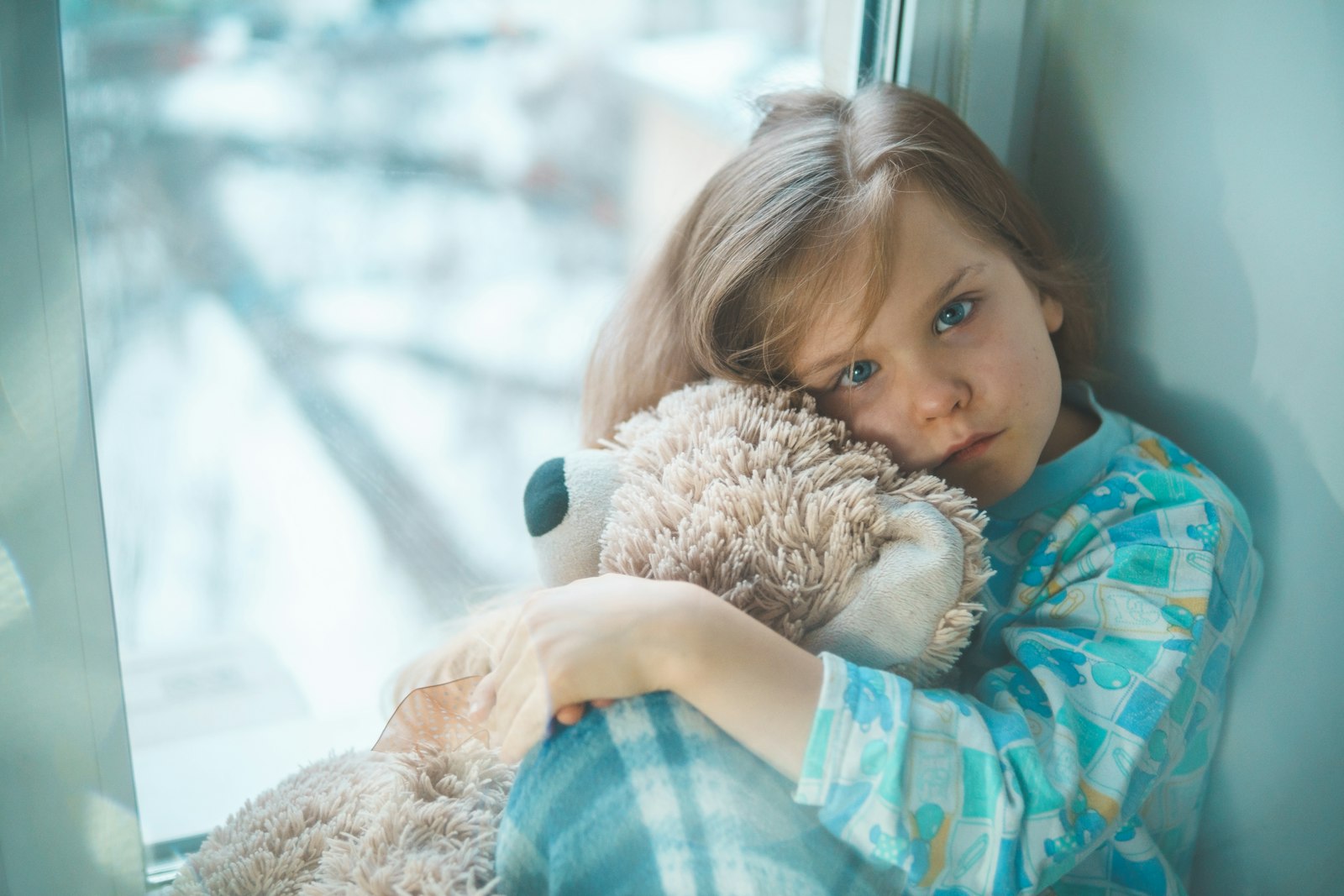 girl in blue white and red plaid shirt hugging brown teddy bear Social Anxiety in Children