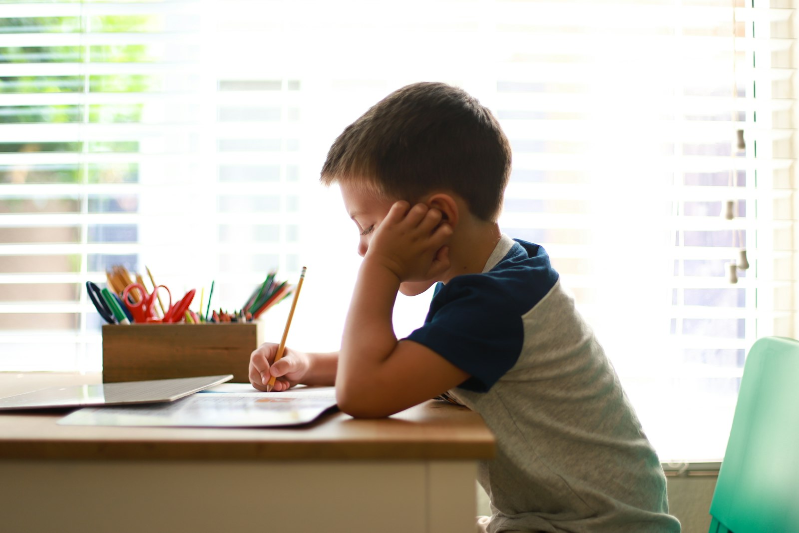 a young boy sitting at a desk writing on a piece of paper Help kids think for themselves