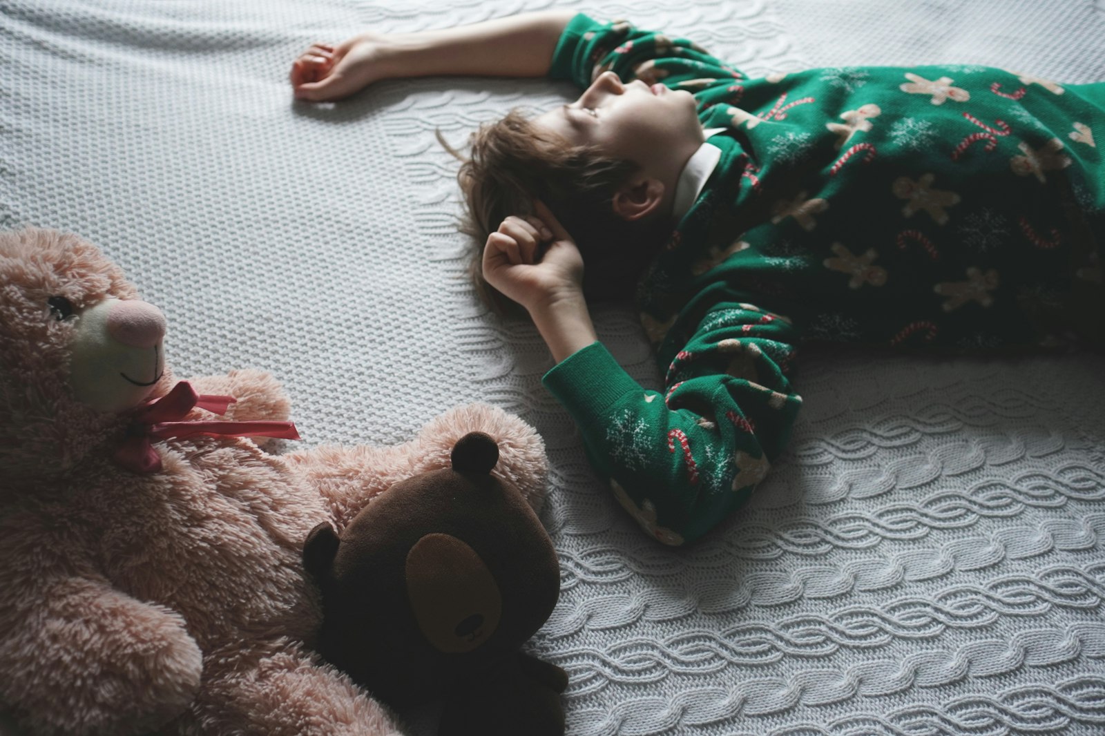 A little boy laying on a bed next to a teddy bear Child Anxiety at Night